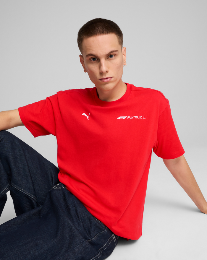 Model seated in a red F1 Essential Relaxed Tee with dark denim jeans, displaying the front logo.
