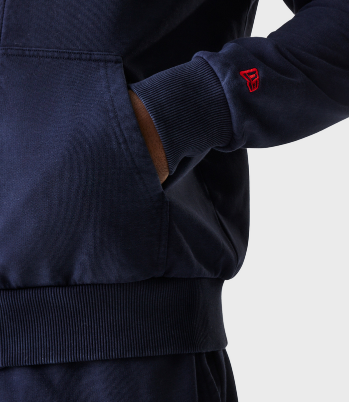 Back view of man in navy oversized hoodie wearing a dark cap with red adjustable strap