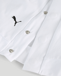 Close-up of white shirt fabric showing a small black Puma logo near the placket and metal snap buttons.