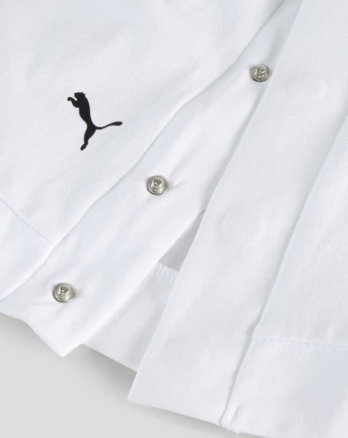 Close-up of white shirt fabric showing a small black Puma logo near the placket and metal snap buttons.