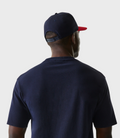 Rear view of a model wearing a navy cap with a red brim over a dark blue T-shirt.
