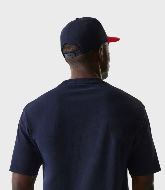 Rear view of a model wearing a navy cap with a red brim over a dark blue T-shirt.