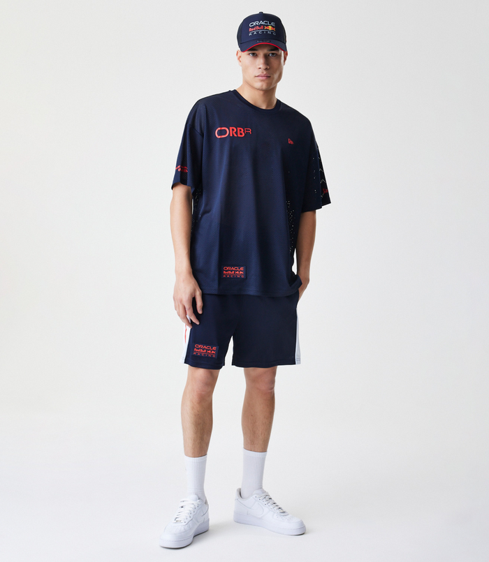 Front view of a male model in the navy mesh tee with red logo patches and white sneakers.