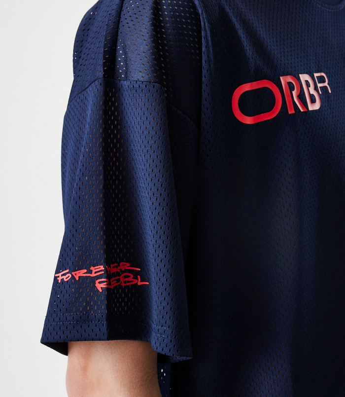 Back view of a navy blue mesh shirt with red Forever REBL lettering and a navy cap with a red strap.