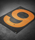 Poster on a dark surface featuring the orange ring and gold blueprint illustrations from the McLaren collection