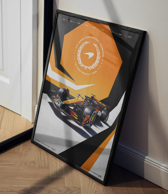 Framed McLaren Formula 1 poster on the floor leaning against a wall in a doorway, showcasing the orange geometric design and a race car.