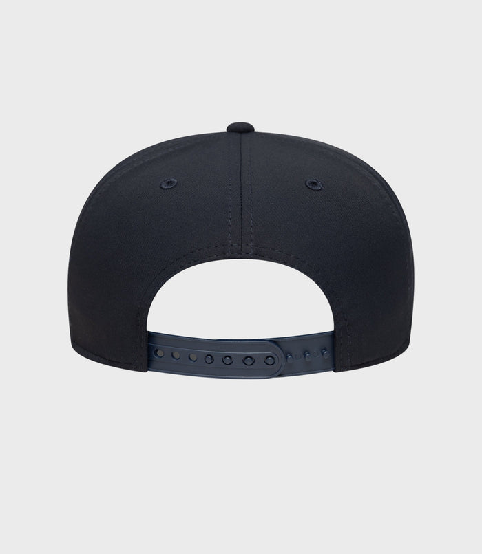 Back view of navy cap with adjustable plastic strap and pink trimmed brim visible.