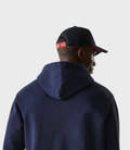 Side profile of a person wearing a dark blue oversized zip hoodie with red hood trim