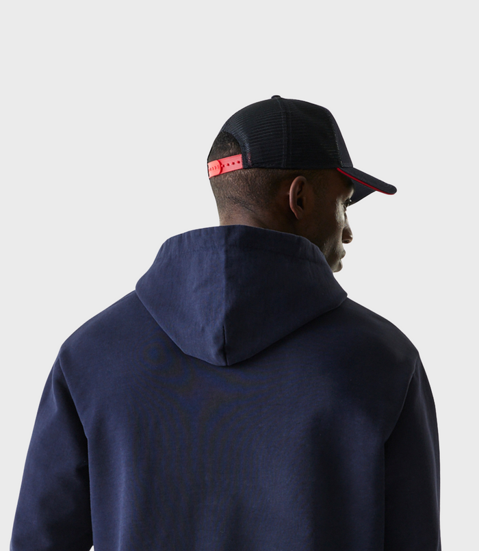 Side profile of a person wearing a dark blue oversized zip hoodie with red hood trim