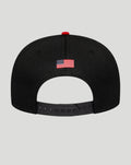 Back view of the cap showing a small American flag patch on the black crown and an adjustable strap with multiple holes