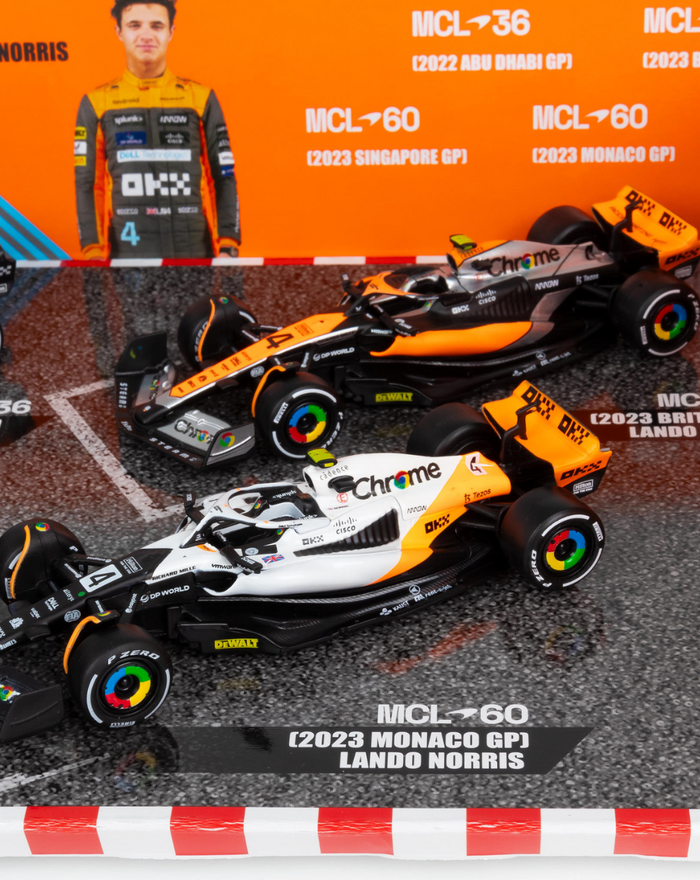 Two McLaren MCL60 F1 cars on a race diorama with Monaco GP signage and a driver cutout.