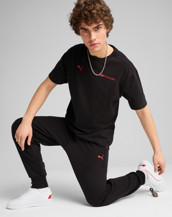 Male model wearing black F1 Essential Relaxed Tee with red Puma logo and Formula 1 branding on chest.