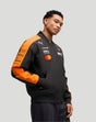 Model wearing a black McLaren Team Bomber Jacket with orange sleeves and multiple sponsor logos