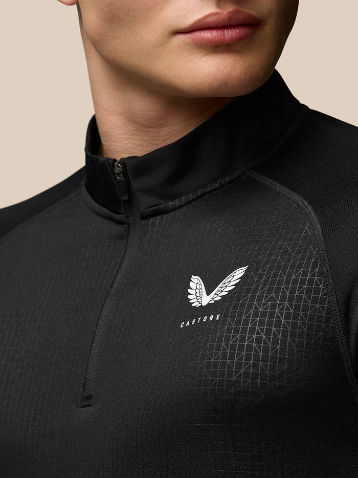 Close-up of a black quarter-zip top with a high stand collar and Castore wing logo on the left chest