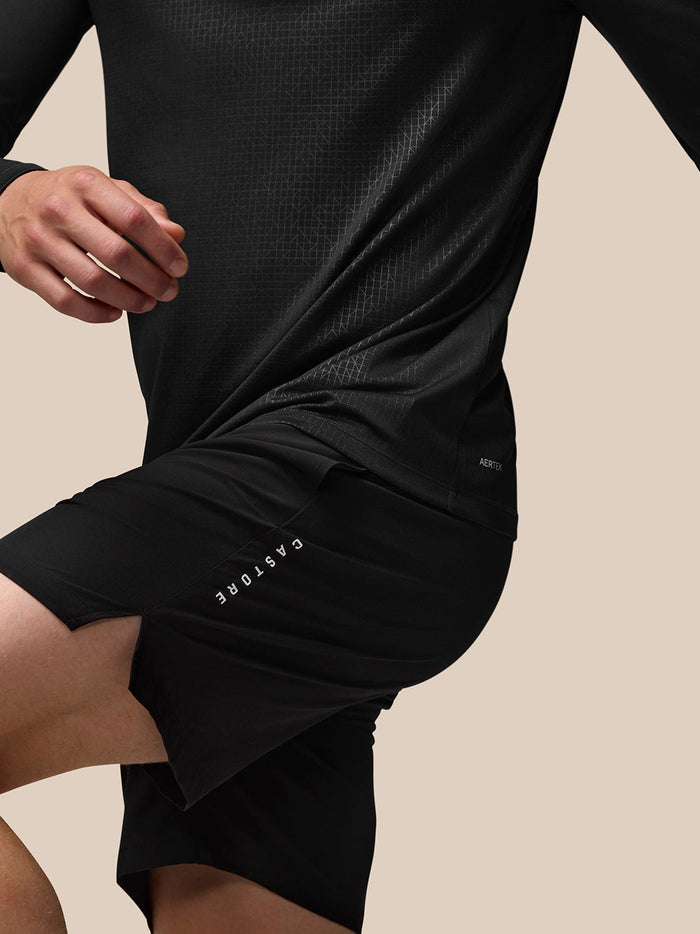 Full body side view of man in black Adapt Print top and shorts with geometric pattern and Castore branding on chest.