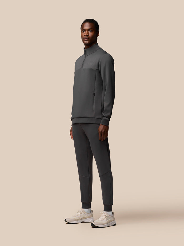 Full-body shot of a male model wearing a charcoal Castore Flex Quarter Zip Top with matching joggers.