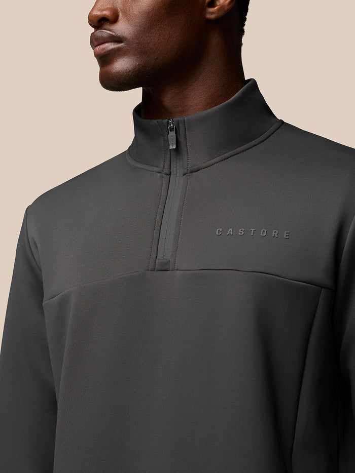 Close-up of charcoal Castore Flex Quarter Zip top on a male model, showing the high collar zip and left chest branding.