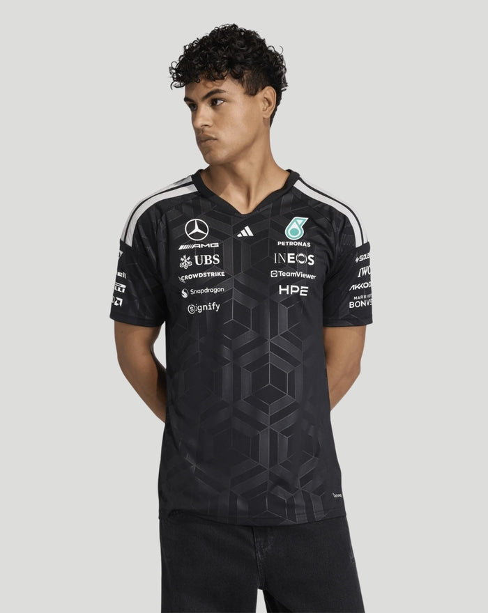 Male model wearing black Mercedes AMG Petronas F1 Team Driver T-Shirt with a geometric pattern and sponsor logos.