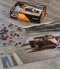 Open McLaren 1000 piece puzzle box with scattered pieces and a race car image on the lid