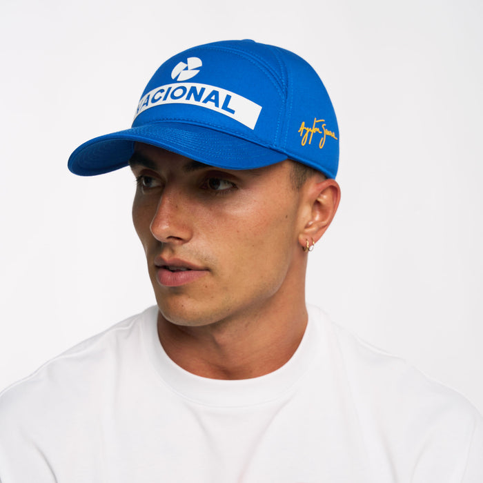 Blue Nacional replica cap worn by model showing white Nacional logo on crown and Senna signature on the side