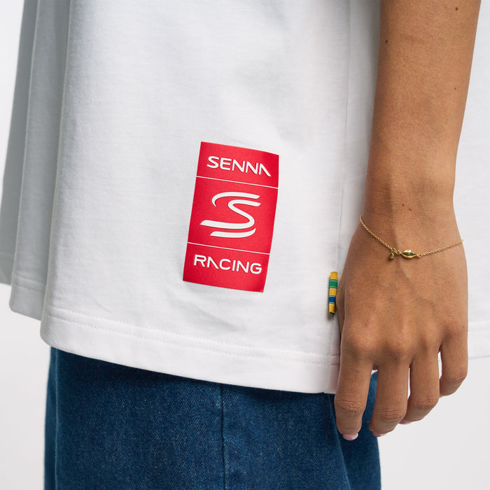 Lower back view of person in white Senna T shirt with red Senna patch at the hem and denim visible