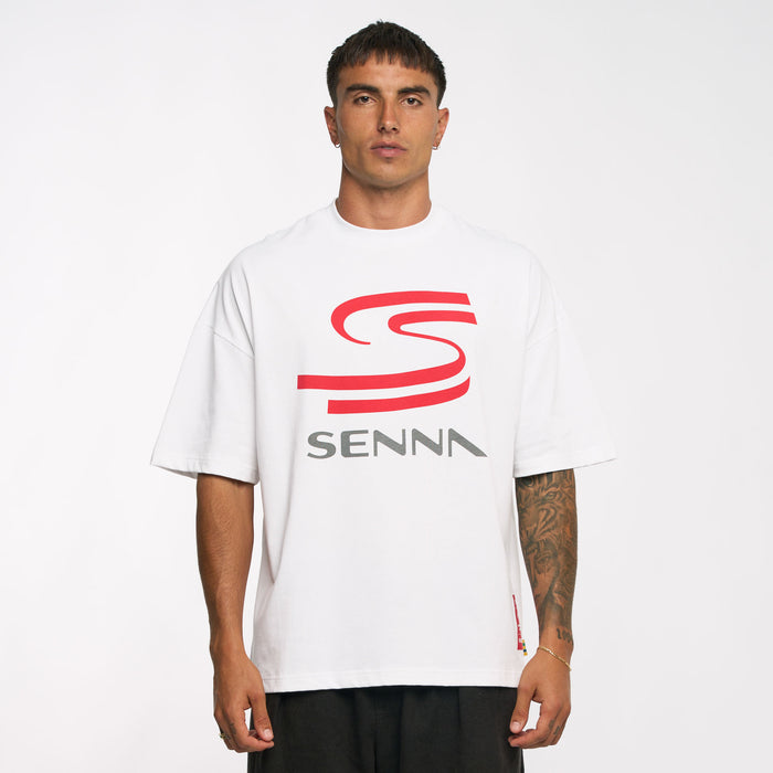 Front view of a model wearing white Ayrton Senna oversized graphic T shirt with bold red chest logo.