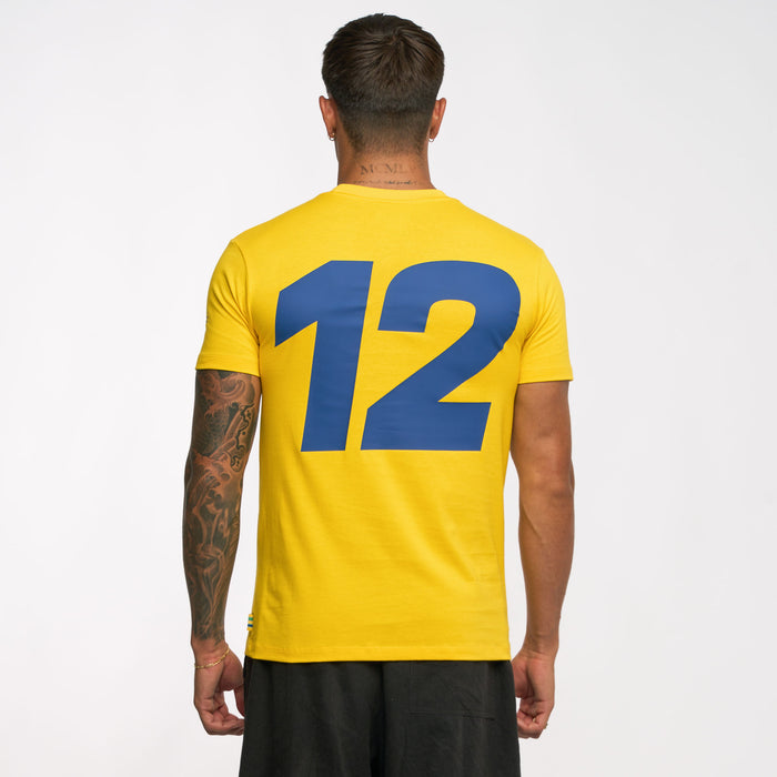 Rear view of a person in a yellow Ayrton Senna retro stripe T shirt showing a large blue number 12 on the back