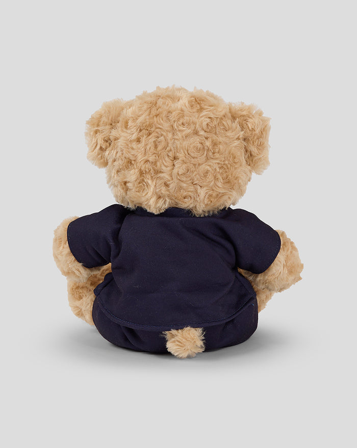 Back view of a soft tan Charlie Bear in a navy outfit showing its fluffy tail