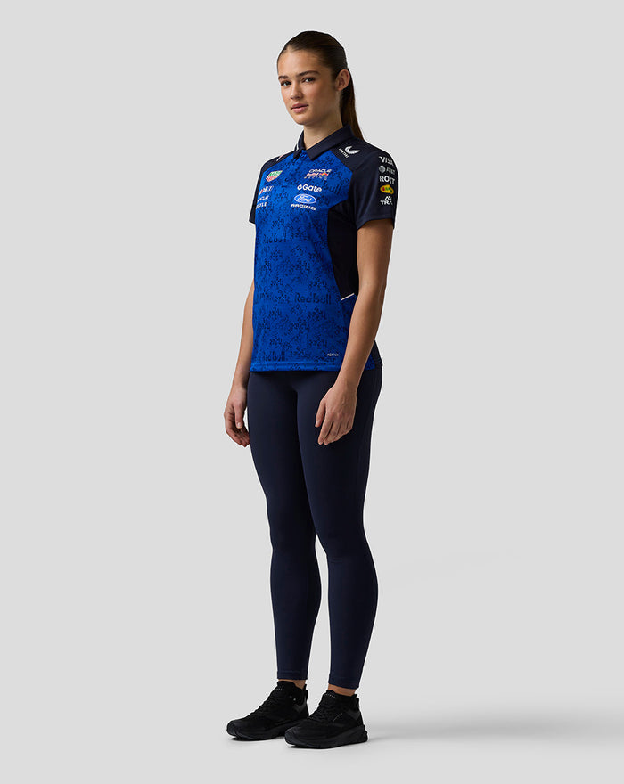 Side profile of a woman wearing a blue Oracle Red Bull Racing team polo with sponsor branding across the chest
