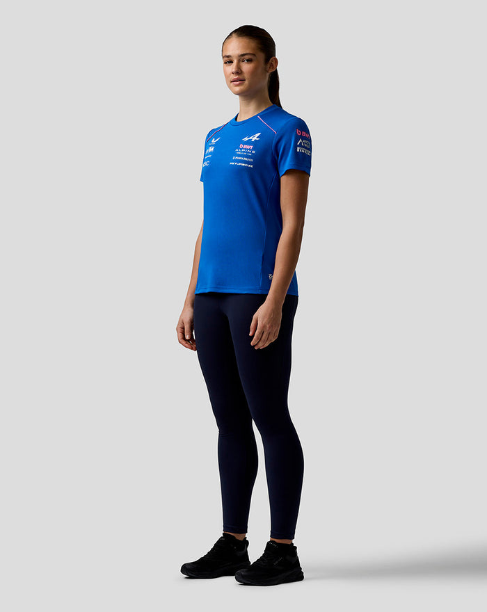 Side profile of a woman in a royal blue BWT Alpine Formula One Team Set Up T Shirt with front logos and pink piping along the shoulder