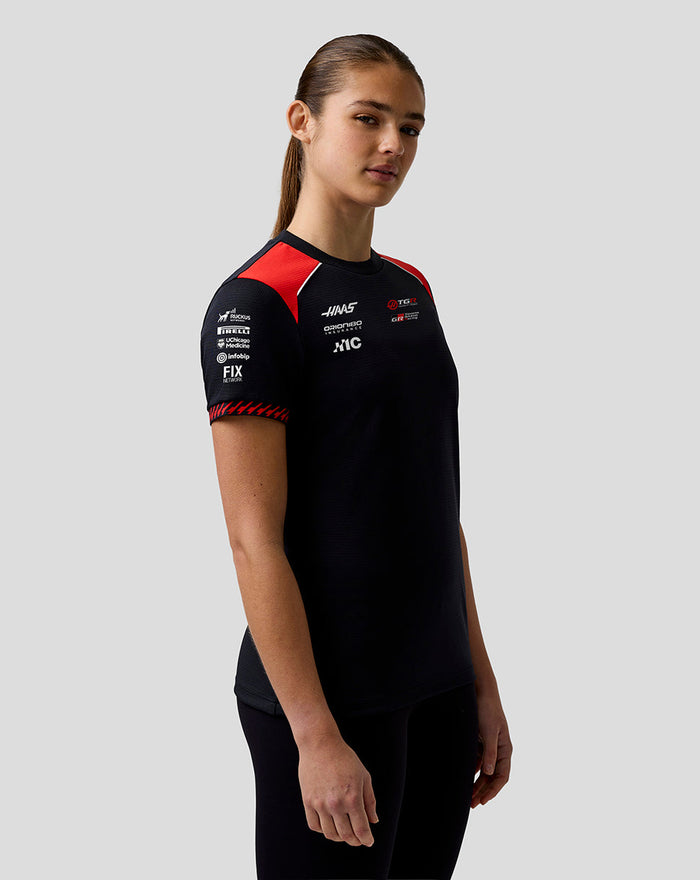 Side profile of a woman in a black Haas Team Driver T Shirt with contrasting red shoulder panels.