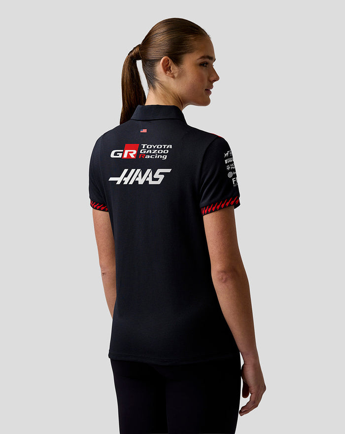 Back view of a female model wearing a dark Haas Team polo with large Haas and GR logos on the back