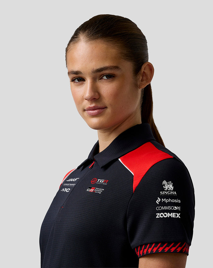 Portrait of a model wearing the Haas Team women's short sleeve polo with dark navy fabric and red shoulder panels with front logos