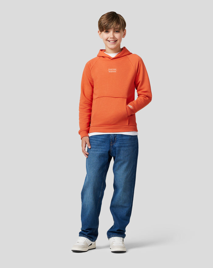 Junior orange rust hoodie with raglan sleeves chest logos and front kangaroo pocket worn by a smiling boy