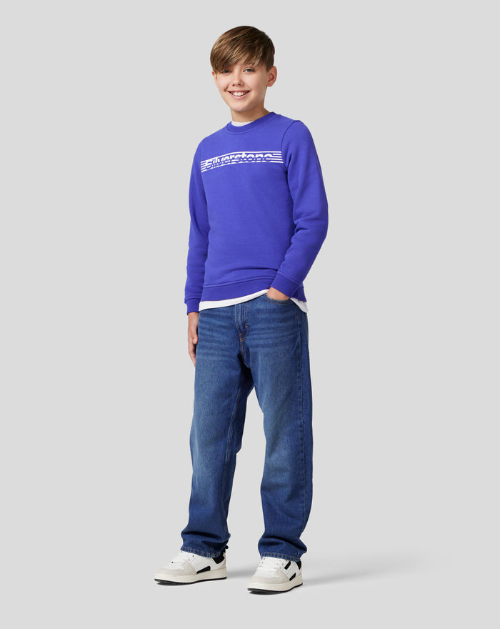 Full body shot of a smiling junior boy wearing a royal blue Junior Silverstone Core Sweatshirt and jeans