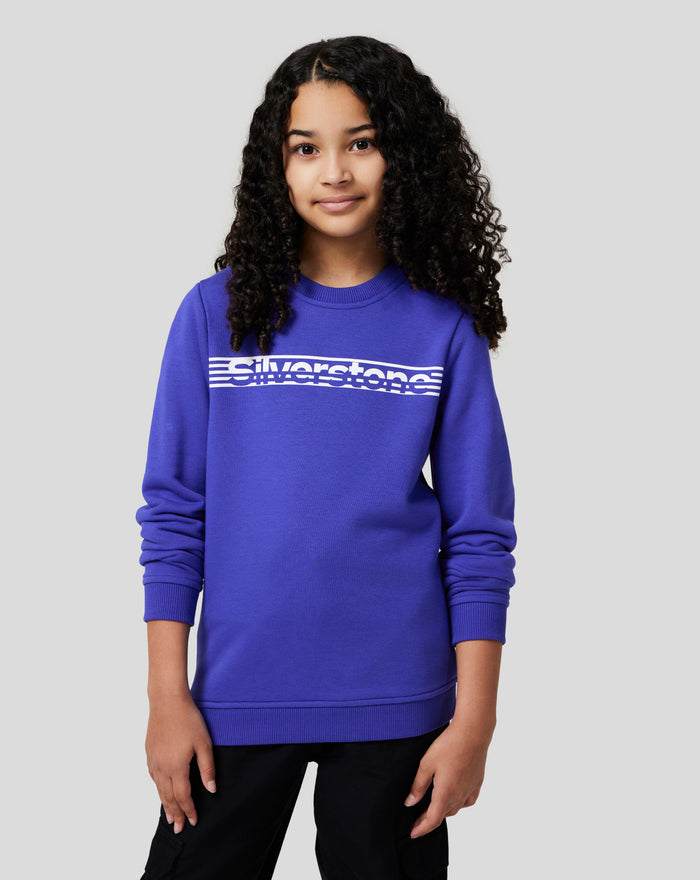 Smiling girl wearing royal blue Junior Silverstone Core Sweatshirt with white logo across chest