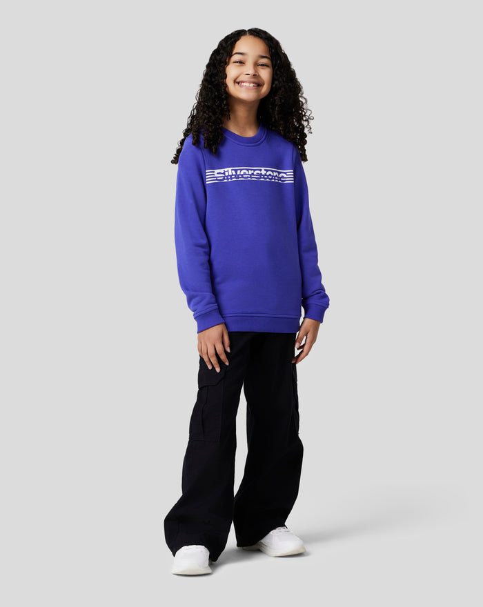Smiling junior girl wearing a royal blue sweatshirt with a white chest graphic standing against a light gray background