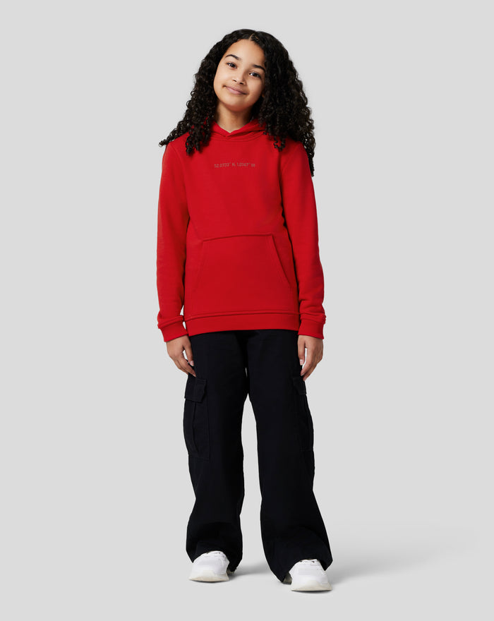 Girl in Junior Silverstone Core Hoodie Racing Red wearing a red fleece hoodie with chest graphic and kangaroo pocket