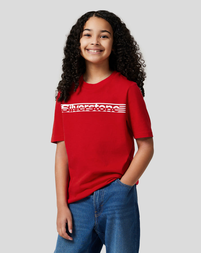 Smiling child wearing a red Junior Silverstone Core T Shirt with a bold white chest graphic.