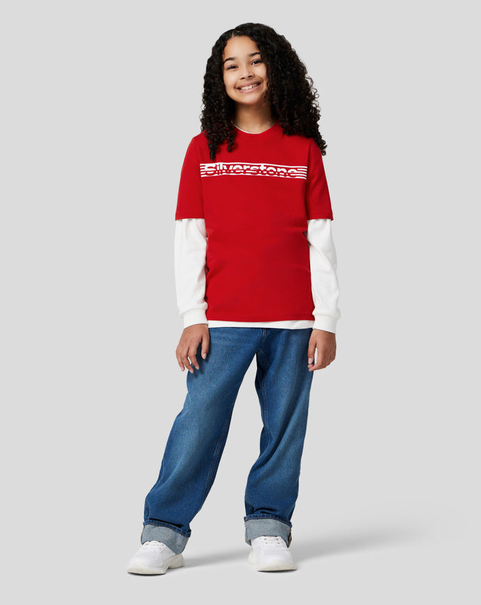 Smiling girl wearing a red Silverstone Core T Shirt with a white striped chest logo and a white long sleeve underneath.
