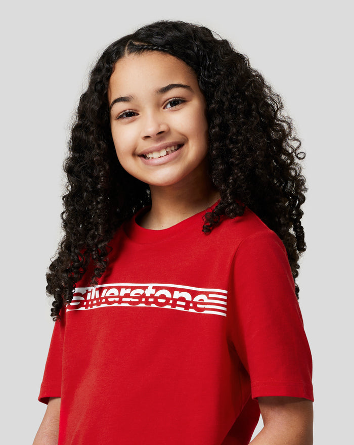 Three quarter front view of a smiling child wearing Racing Red Silverstone Core T-Shirt with bold white chest graphic