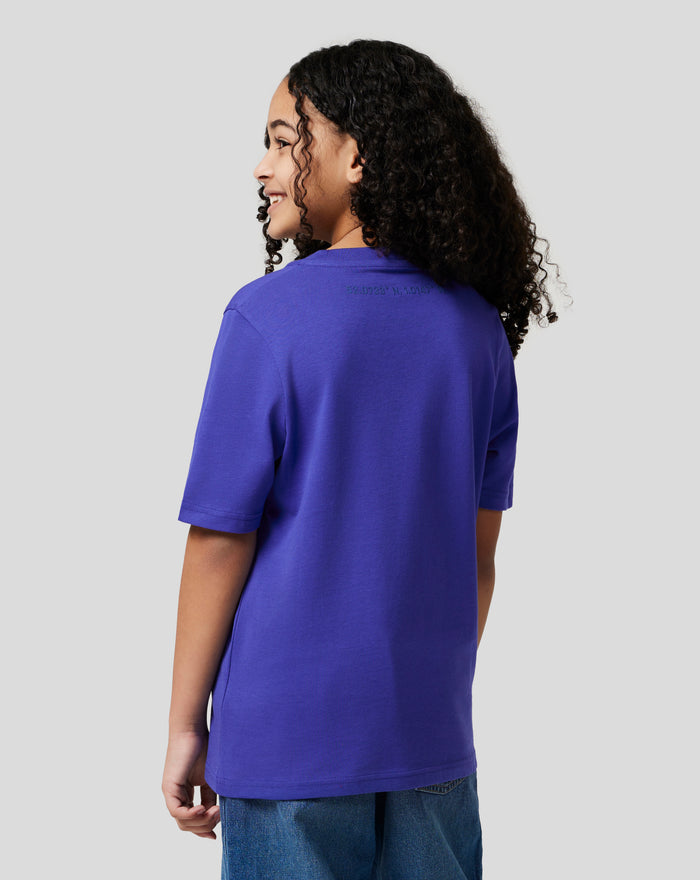 Side view of a young model wearing a royal blue Junior Silverstone Core Graphic T Shirt against a light gray background.