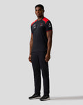 Three-quarter rear view of a model wearing the Haas Team Driver T Shirt, black with red chevron cuff details on the sleeves.