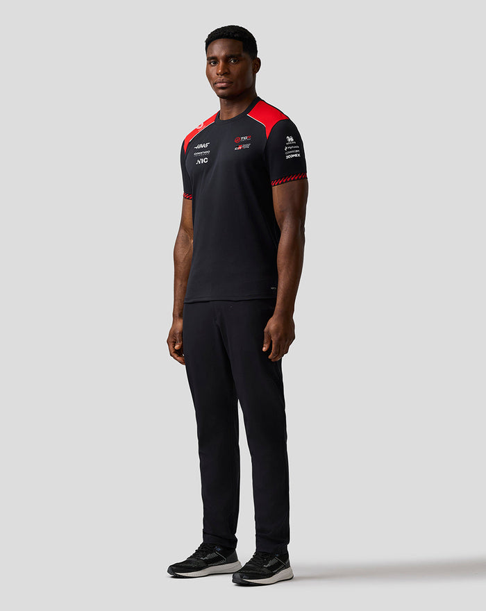 Three-quarter rear view of a model wearing the Haas Team Driver T Shirt, black with red chevron cuff details on the sleeves.