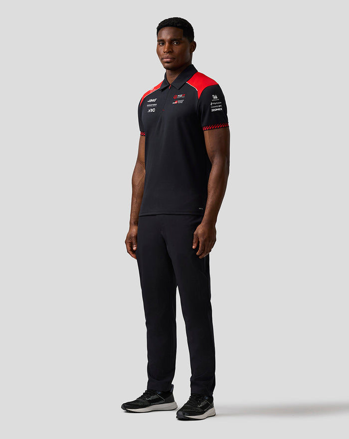 Male model wearing Official Haas Team Short Sleeve Polo Shirt in black with red shoulder panels and sponsor logos.