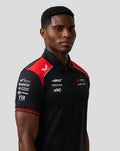 Close-up of male model wearing Haas Team polo with red shoulder panels and multiple sponsor logos on the chest.