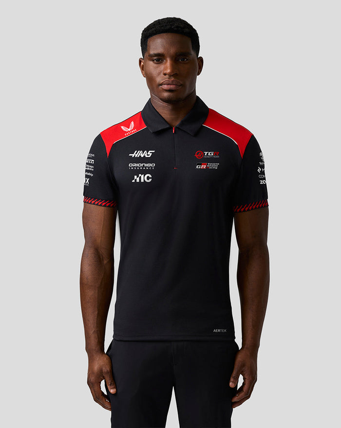 Front view of male model in Haas Team polo with red shoulder panels and prominent sponsor branding on the chest.