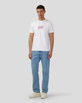 Full body shot of a man in a white Silverstone x Castore Festival Graphic T-Shirt with the chest graphic, paired with blue jeans and beige sneakers