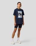 Full body view of a model in a navy Silverstone Core Track Graphic T Shirt with a large front graphic, paired with black shorts and white sneakers.