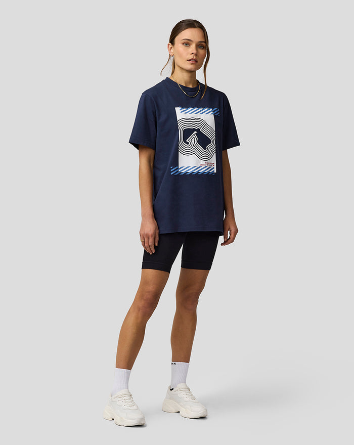 Full body view of a model in a navy Silverstone Core Track Graphic T Shirt with a large front graphic, paired with black shorts and white sneakers.